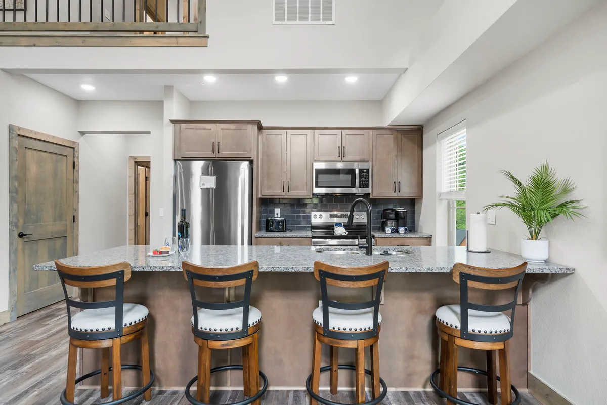 An inviting kitchen scene with a central island topped with granite, surrounded by bar stools and equipped with stainless steel appliances. Natural light pours in, and the space is neat, modern, and welcoming—ideal for both casual family breakfasts and celebratory dinners.