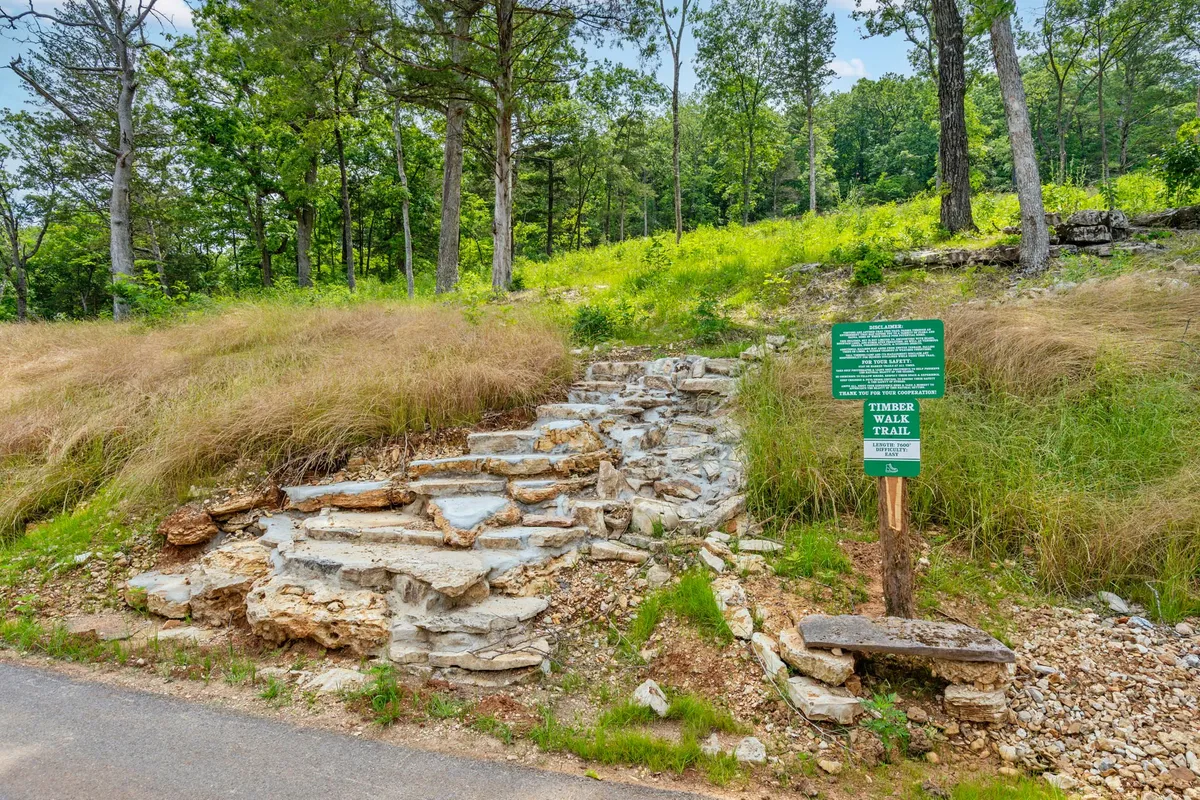 A stone trail marked by a sign weaves through lush greenery, inviting visitors to embark on a scenic nature walk or hike. The natural foliage and clear pathway capture the adventurous spirit of the outdoors just beyond the lodge.