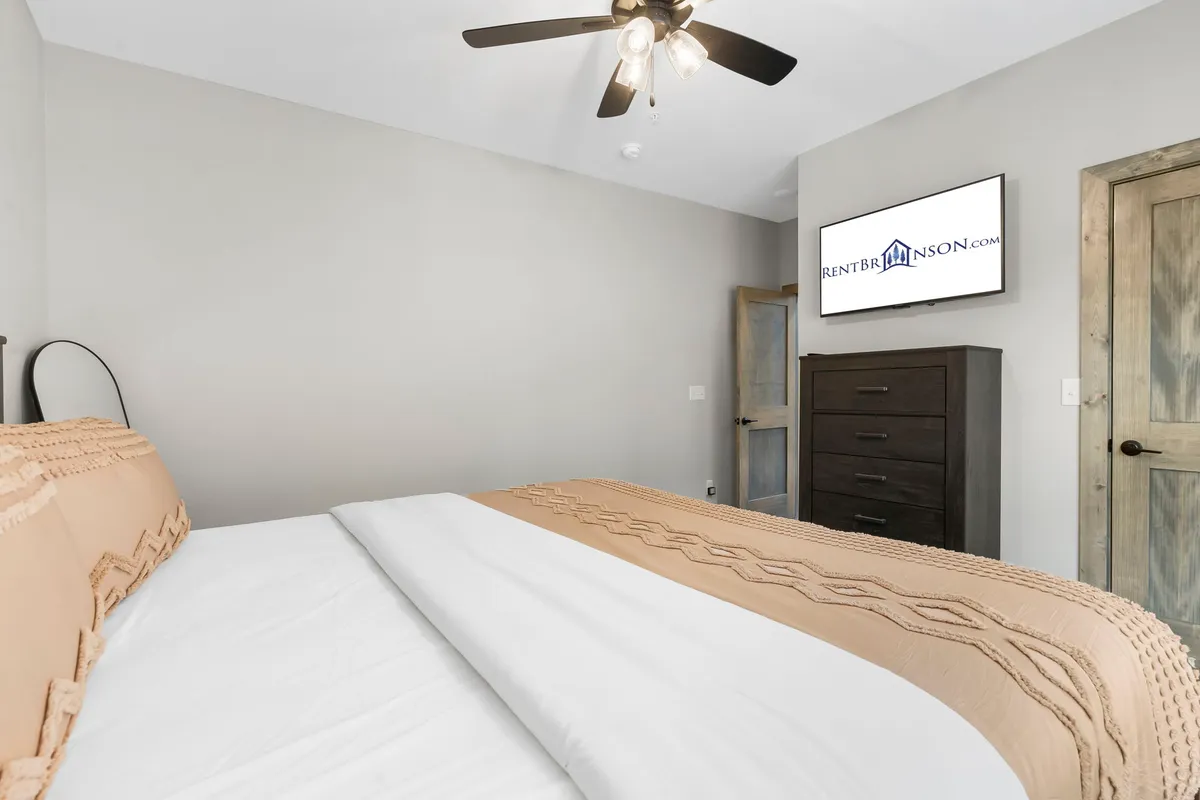 A restful bedroom with a comfortable bed, nightstand, wall-mounted television, and a door leading to a private ensuite. Soft, neutral decor and gentle lighting create a cozy, inviting environment perfect for relaxation and unwinding after a day outdoors.