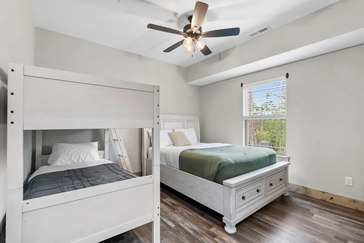 A cozy bedroom featuring a queen bed and a twin bunk bed, complemented by a window that brings in natural light. The arrangement is ideal for families or groups needing flexible sleeping arrangements, with a warm and inviting mood.