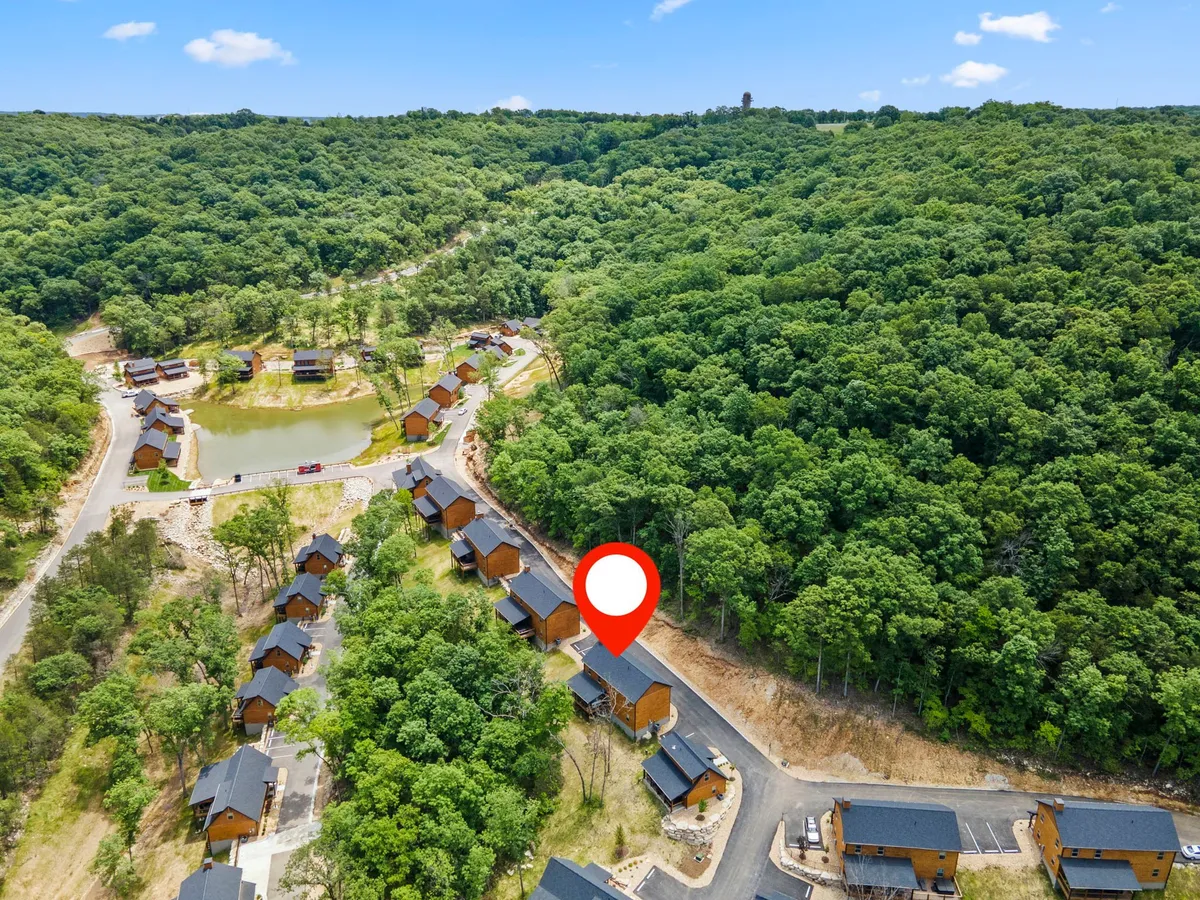 This exterior image showcases multiple wooden cabins nestled among greenery, with a tranquil pond and a winding road visible. The setting emphasizes a peaceful, nature-rich environment ideal for family walks, fishing, and outdoor gatherings.