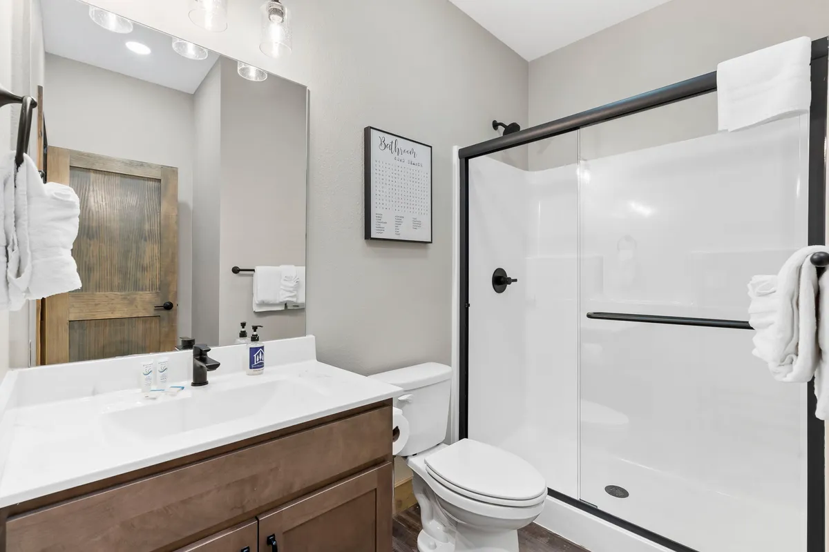 A modern ensuite bathroom with a vanity, sink, shower enclosure, and a large mirror, all bathed in inviting, fresh light. The space is organized for personal care and relaxation, supporting the sense of privacy and comfort described.