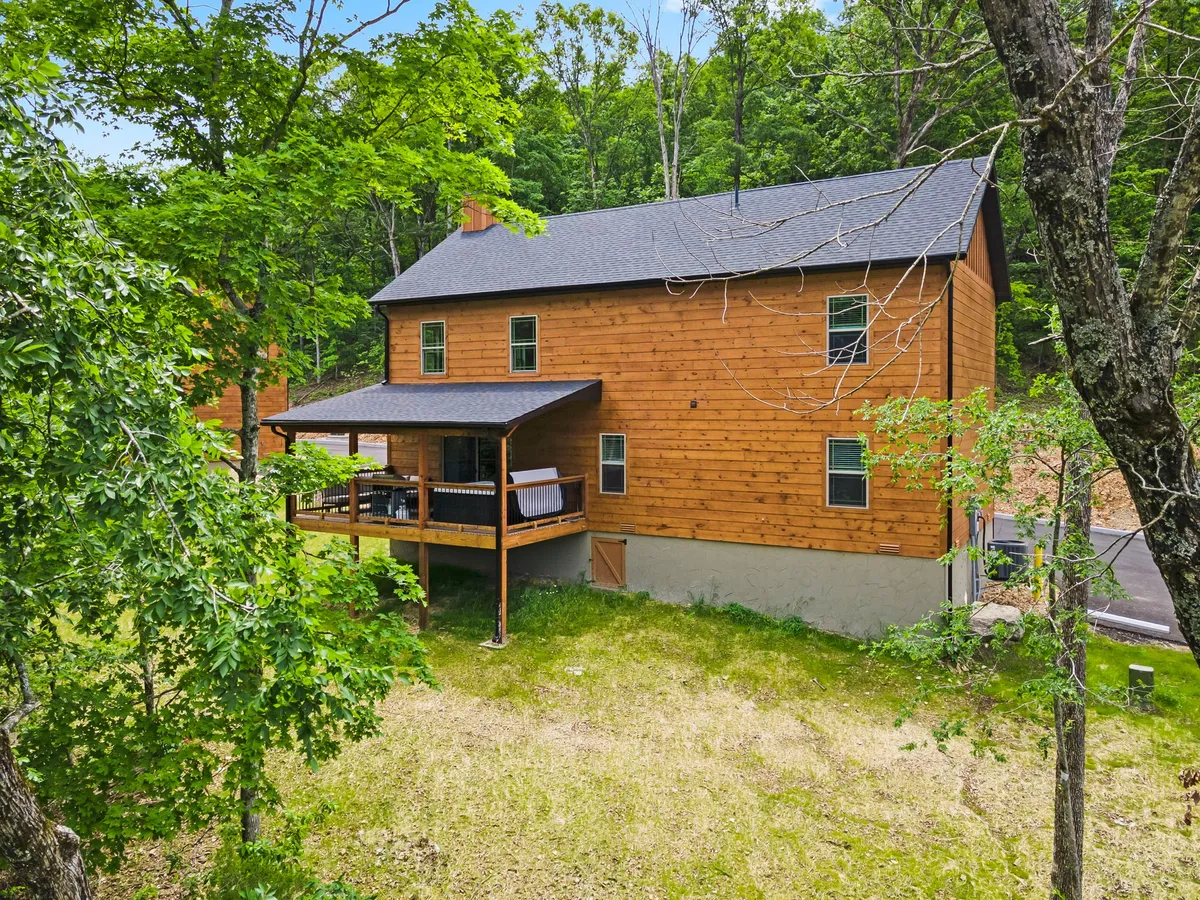 A tranquil deck area attached to a wooden house, surrounded by tall trees. The deck is furnished for relaxation, inviting guests to enjoy the outdoors, whether it's morning coffee or stargazing at night. The natural setting is peaceful and private, emphasizing the retreat's connection to nature.